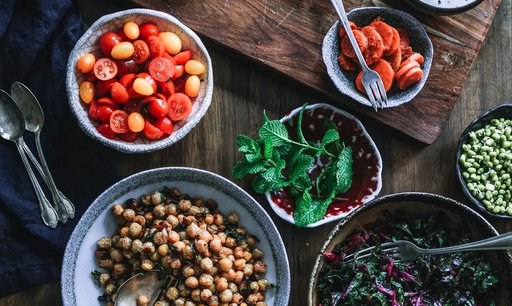 Assorted vegan plant-based foods in bowls: cherry tomatoes, chick peas, mustard greens